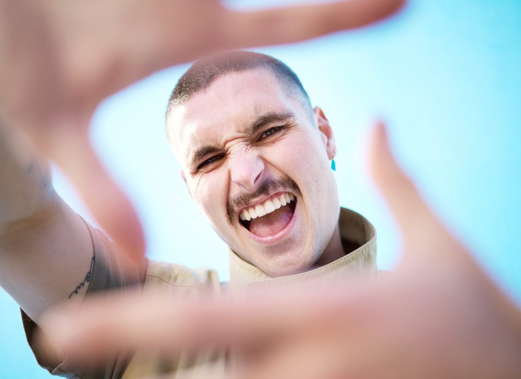 Attractive young man holding hands in front of his face to frame his face for the camera. The male G-spot: getting a prostate massage.