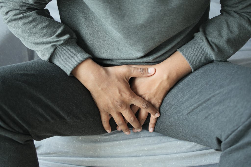 Young man holds hands in front of his pelvis: the concept of prostate and bladder problem, crotch pain. The male G-spot: getting prostate massage.