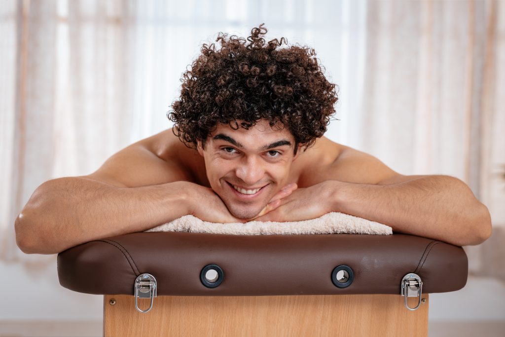 Attractive male laying on a massage table with a smile. How to Give Him the Best Sensual Erotic Massage.